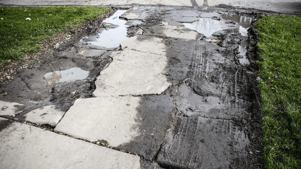 A very broken, old driveway covered in mud and tire tracks.