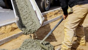 Concrete pours from a slide onto the work site where a worker smooths it out.